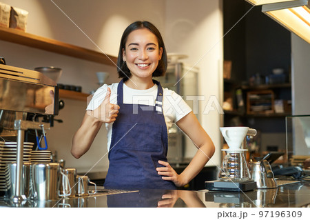 Smiling asian barista, girl in cafe uniform, shows okay sign, recommends their coffee, approve new flavours, standing in apron 97196309