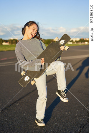 Funny asian girl enjoying skating, holding skateboard like guitar and shadow playing, having fun outdoors Funny asian girl enjoying skating, holding skateboard like guitar and shadow playing, having fun outdoors 97196310