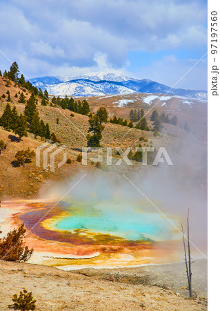 View of steamy hot spring from above overlooking snowy mountains by Yellowstone 97197560