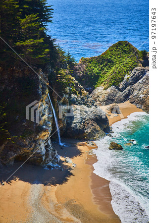 View of hidden waterfall from cliffs into sandy beaches by ocean waves View of hidden waterfall from cliffs into sandy beaches by ocean waves 97197643