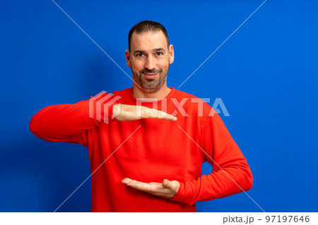 A man holding an object with both hands in front of him, displaying, offering or advertising an object against a blue wall. Empty. Space. Concept. Object. Background. Portrait. Copy A man holding an object with both hands in front of him, displaying, offering or advertising an object against a blue wall. Empty. Space. Concept. Object. Background. Portrait. Copy 97197646