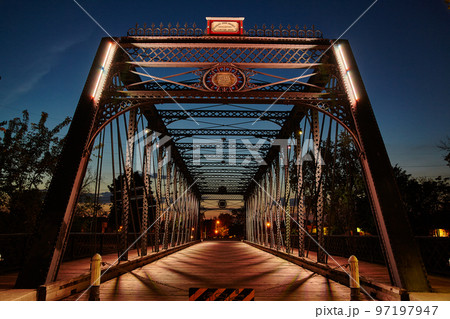 Metal bridge leading into downtown lit by street lamplight at dusk Metal bridge leading into downtown lit by street lamplight at dusk 97197947