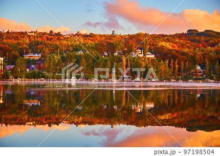 Sail boats and other boats docked on a shoreline bathed in fall colors and with a river reflecting the scene 97198504
