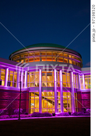 Head on shot of the front door of the modern building with many windows at twilight lit up purple Head on shot of the front door of the modern building with many windows at twilight lit up purple 97198520