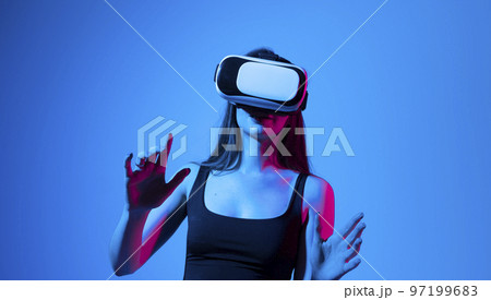Portrait of brunette woman in a black top with 3D virtual reality glasses enjoys his trip in an adventurous world in neon light. Concept of connection technology with science, augmented reality. Portrait of brunette woman in a black top with 3D virtual reality glasses enjoys his trip in an adventurous world in neon light. Concept of connection technology with science, augmented reality. 97199683