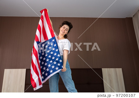 A young happy woman dances with an American flag. Bottom view. Indoor. The concept of the American national holidays and patriotism 97200107