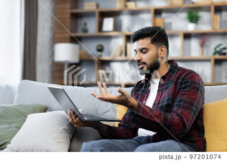 Young bearded businessman in checkered red shirt working on laptop computer, talking online Young bearded businessman in checkered red shirt working on laptop computer, talking online 97201074