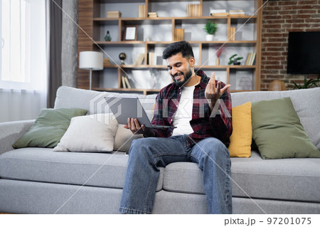 Young bearded businessman in checkered red shirt working on laptop computer, talking online 97201075