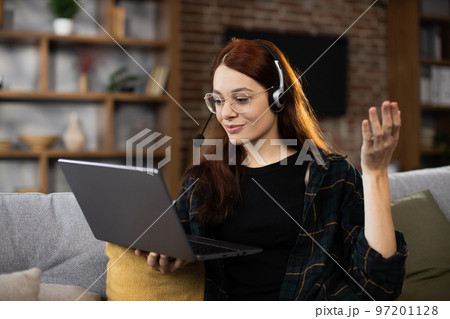 Closeup of young student woman in wireless headset watching online lesson on laptop Closeup of young student woman in wireless headset watching online lesson on laptop 97201128