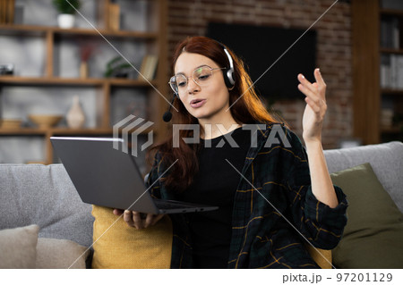 Closeup of young student woman in wireless headset watching online lesson on laptop 97201129