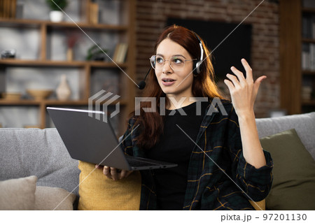 Closeup of young student woman in wireless headset watching online lesson on laptop 97201130