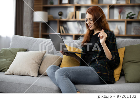 Smiling young woman using laptop, sitting on couch at home, beautiful girl having video call Smiling young woman using laptop, sitting on couch at home, beautiful girl having video call 97201132