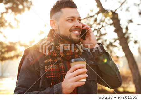 Man with cup of coffee talking on smartphone in morning outdoors Man with cup of coffee talking on smartphone in morning outdoors 97201565