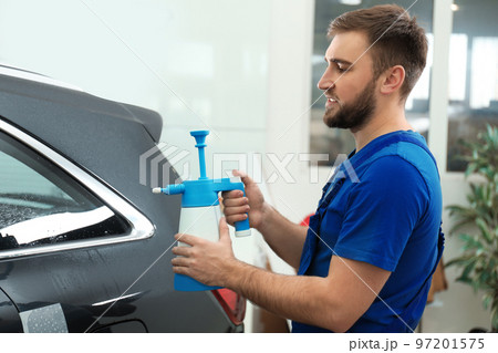 Worker spraying water onto car window before tinting 97201575