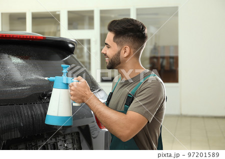 Worker spraying water onto car window before tinting 97201589