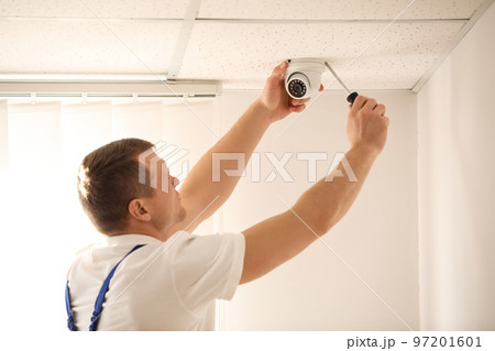 Technician installing CCTV camera on ceiling indoors 97201601