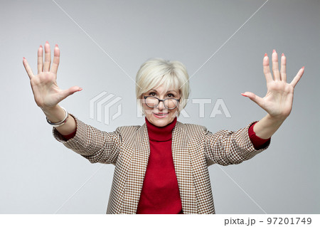 beautiful elderly woman with glasses holds her hands in front of her with open palms facing the camera. advertising concept of a business woman leader beautiful elderly woman with glasses holds her hands in front of her with open palms facing the camera. advertising concept of a business woman leader 97201749