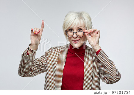 beautiful elderly woman with glasses shows her index finger up. advertising concept of a business woman leader beautiful elderly woman with glasses shows her index finger up. advertising concept of a business woman leader 97201754