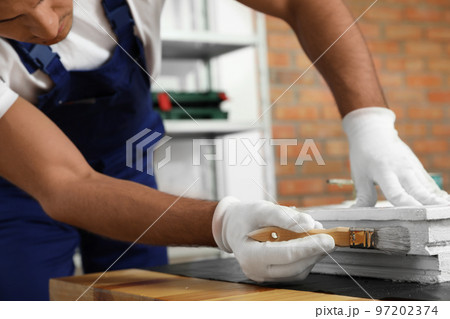 Repairman painting old window at table indoors, closeup 97202374