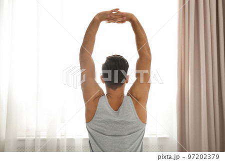 Man stretching near window at home. Lazy morning 97202379