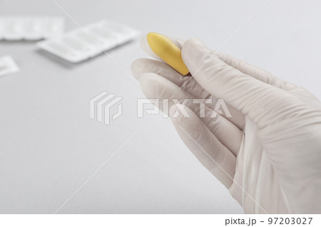 Woman holding suppository on light background, closeup. Hemorrhoid treatment 97203027