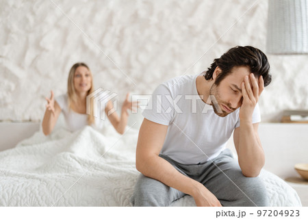 Angry woman shouting at her husband, having conflict while sitting on bed at home, focus on upset man 97204923
