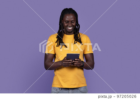 Joyful stylish young black guy using digital tablet on purple Joyful stylish young black guy using digital tablet on purple 97205026