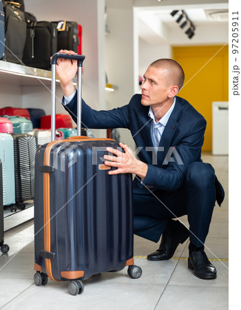 Portrait of man picking new big plastic luggage bag with wheels Portrait of man picking new big plastic luggage bag with wheels 97205911