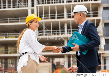 Woman client shaking hand with builder at construction site Woman client shaking hand with builder at construction site 97206243