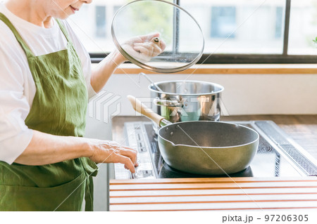 家のキッチンでIHクッキングヒーターを使って料理を作るアジア人の高齢者女性 97206305