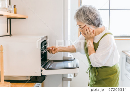 家のキッチンで料理を作るため電子レンジを使うアジア人の高齢者女性（困る） 97206314