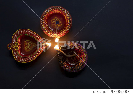 Happy Diwali. Three clay dia lamps are burning on a black background. Deepa festival of Hindus. Can be used for advertising banner, poster background Happy Diwali. Three clay dia lamps are burning on a black background. Deepa festival of Hindus. Can be used for advertising banner, poster background 97206403