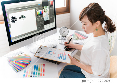 データを見ながらロゴデザインをするグラフィックデザイナーの女性 97206911