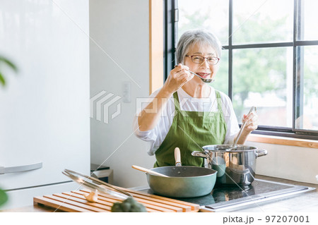 家のキッチンで料理を作って味見するアジア人の高齢者女性（笑顔） 97207001