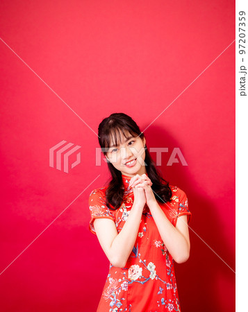 美しい女性はチャイナ ドレスを着て、赤い背景で笑顔します。 97207359