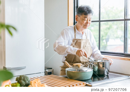 家のキッチンでフライパンを使って手料理を作るアジア人の高齢者男性（笑顔） 97207706