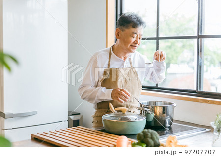 家のキッチンで料理を作って味見するアジア人の高齢者男性（笑顔） 97207707