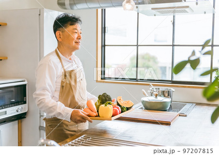 家のキッチンで野菜を使って料理するアジア人中高年・高齢者男性 97207815