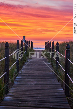 Orange and red sunrise light with straight boardwalk path guiding you to beach 97208355