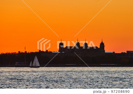 Silhouette of Ellis Island with boat sailing past and intense orange sky 97208690