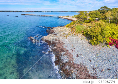 Aerial of blue waters over Maine coastline with forest and pier in background 97208774