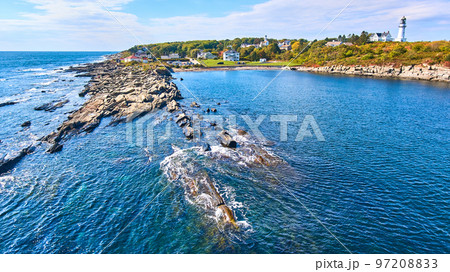 Rocky coastline from over water in Maine with lighthouse in background 97208833