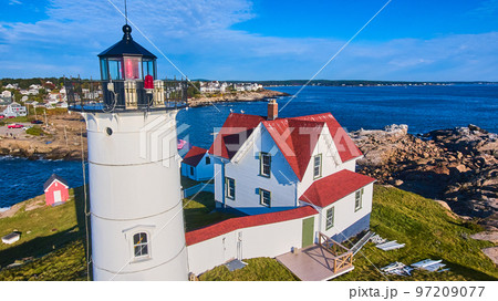 Up close aerial of lighthouse in Maine on island with town of homes in background 97209077