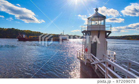 Large commercial ship on Maine river sails past small lighthouse with blue skies 97209078