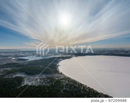 Snow-covered forest on lake shore with ice at sunset and the city on horizon, auerial view 97209986