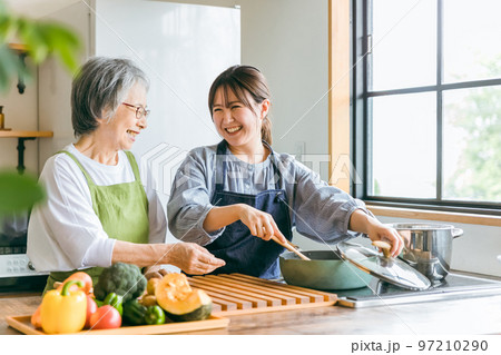 家のキッチンで一緒に料理・家事・自炊をする笑顔のアジア人高齢者女性と若い女性（家政婦・家事代行） 97210290