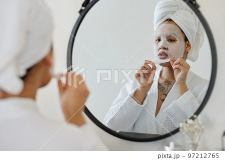 Young African American woman taking hydrating sheet mask off her face 97212765