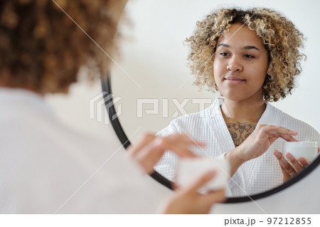 Young gorgeous woman looking in mirror while going to apply cream on her face 97212855