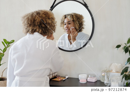 Young pretty woman in white bathrobe applying refreshening toner on face Young pretty woman in white bathrobe applying refreshening toner on face 97212874