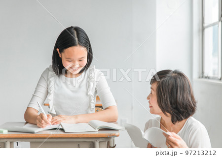 夏期講習で教科書を見ながら教える塾講師・先生と疑問を質問する小学生・中学生・高校生の生徒(子供) 夏期講習で教科書を見ながら教える塾講師・先生と疑問を質問する小学生・中学生・高校生の生徒(子供) 97213212